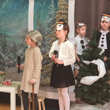 Pieciu aktorow w teatrzyku. Chlociec trzyma mikrofon, W tle zimowy krajobraz i choinka