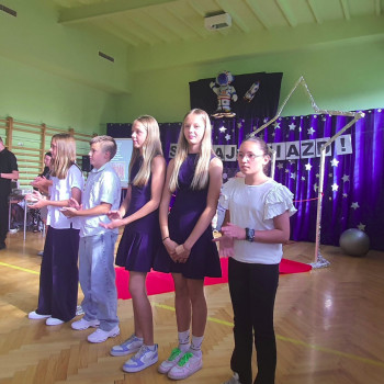 Uczniowie stojący na scenie i klaszczący, podczas gali laureatów