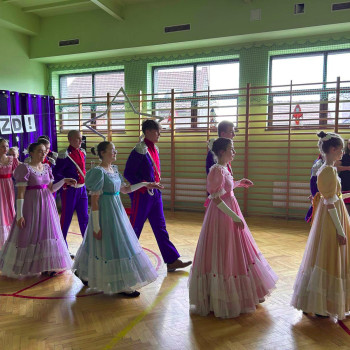 Uczniowie ubrani w stroje stylizowane na historyczne, idący w rzędzie na scenie podczas gali