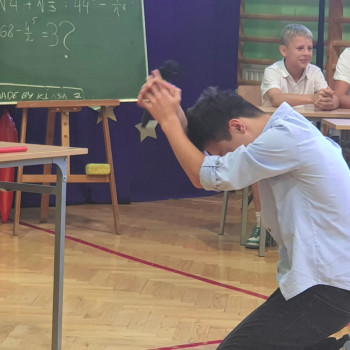 Uczniowie podczas przedstawienia uczeń klęczy przed biurkiem